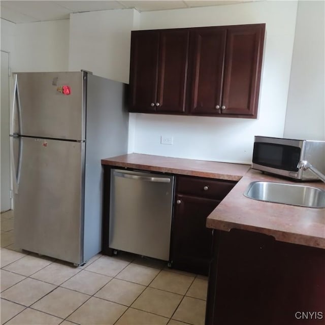 kitchen with light tile patterned floors, dark brown cabinetry, a sink, and appliances with stainless steel finishes