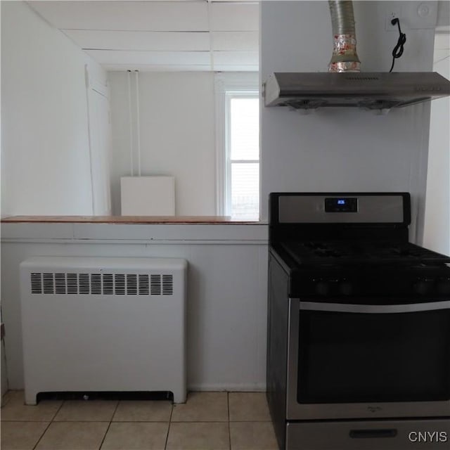 kitchen featuring radiator heating unit, light tile patterned floors, ventilation hood, and gas range