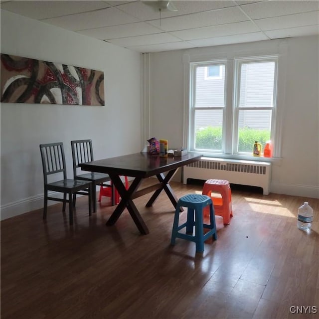 dining area with baseboards, radiator heating unit, wood finished floors, and a paneled ceiling