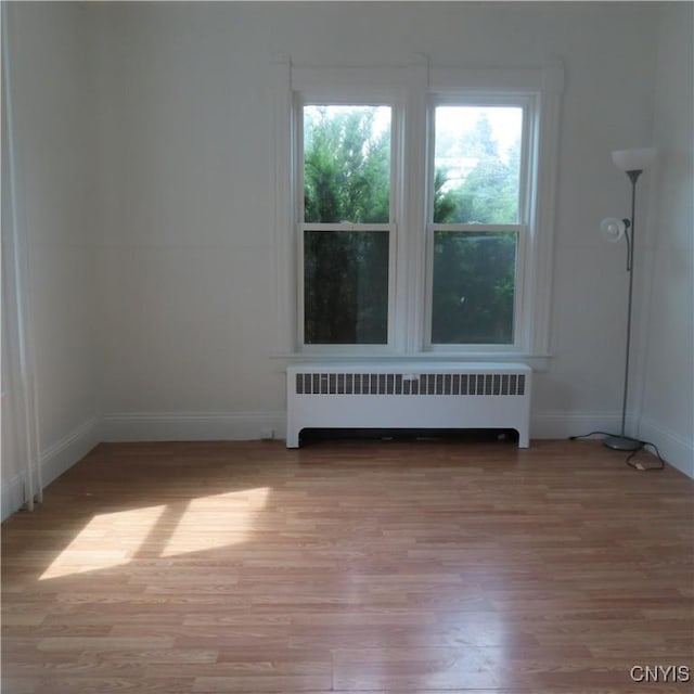 empty room featuring baseboards, radiator heating unit, and light wood-style floors