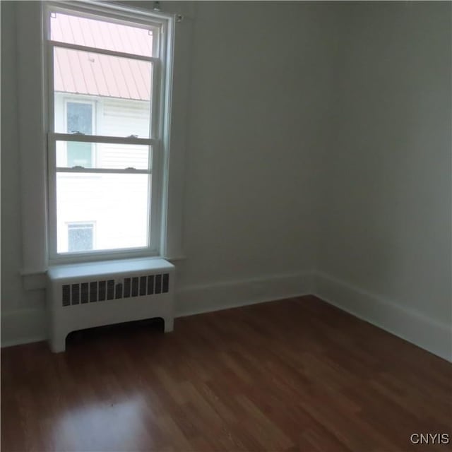 unfurnished room with dark wood-style floors, radiator heating unit, and baseboards