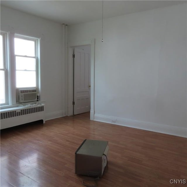 spare room with baseboards, radiator, cooling unit, and wood finished floors