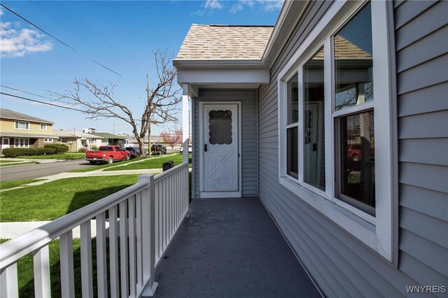doorway to property with a porch, a lawn, a shingled roof, and a residential view