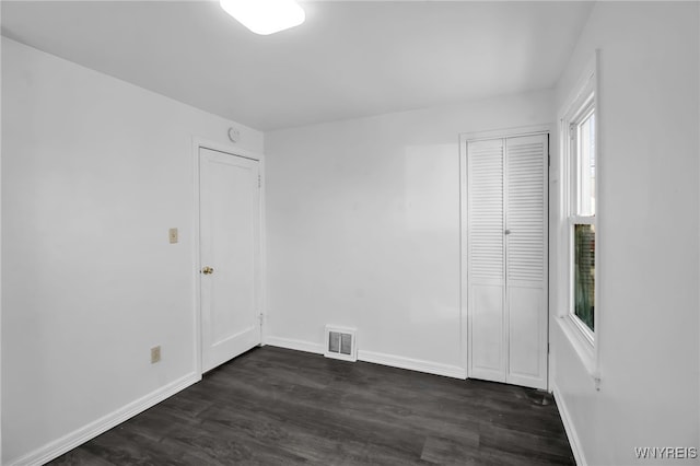 empty room with dark wood-type flooring, visible vents, and baseboards