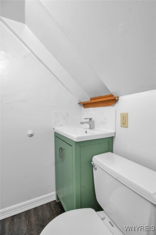 half bathroom with toilet, vanity, lofted ceiling, and wood finished floors