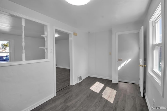 unfurnished room featuring dark wood-style floors, visible vents, baseboards, and a healthy amount of sunlight
