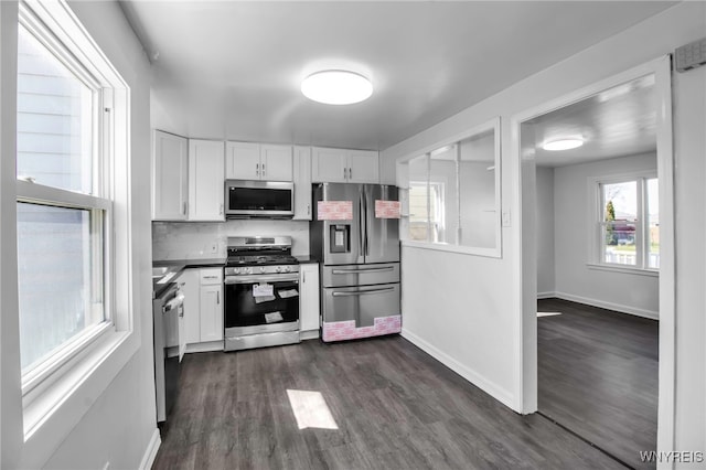 kitchen featuring dark wood finished floors, tasteful backsplash, stainless steel appliances, white cabinets, and dark countertops