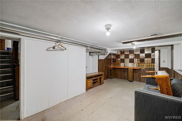 finished basement featuring light floors, a textured ceiling, wooden walls, and a bar