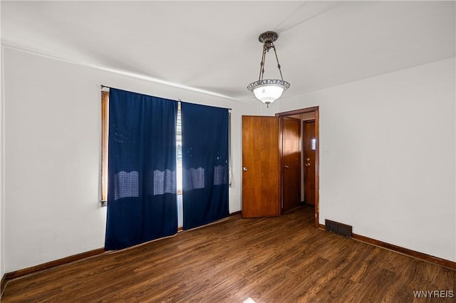 empty room with baseboards, visible vents, and wood finished floors