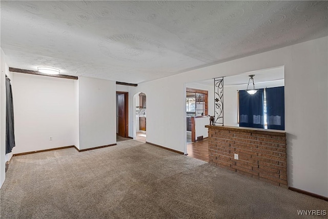 empty room featuring baseboards, arched walkways, a textured ceiling, and carpet flooring