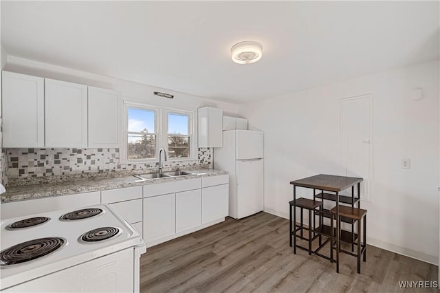 kitchen featuring light wood finished floors, a sink, decorative backsplash, white appliances, and white cabinets