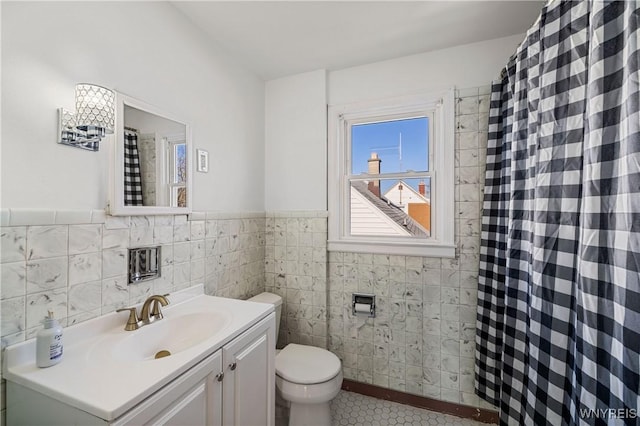 bathroom featuring tile patterned flooring, wainscoting, tile walls, toilet, and vanity