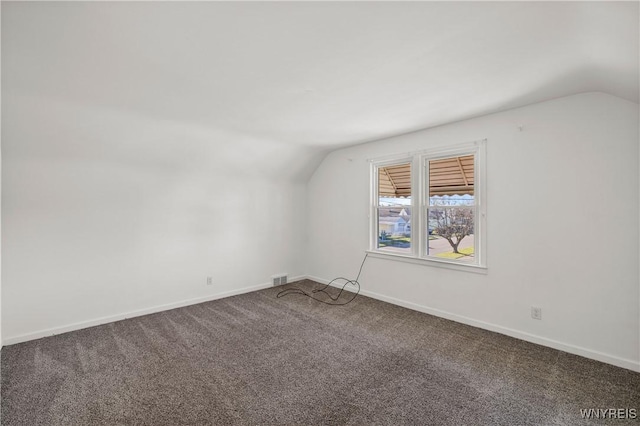 carpeted spare room featuring baseboards, visible vents, and vaulted ceiling