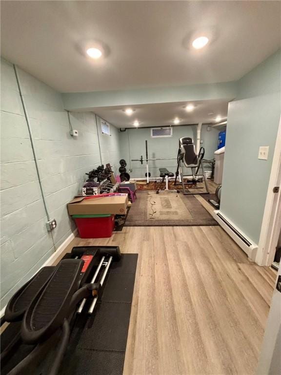 exercise room with wood finished floors, concrete block wall, and a baseboard radiator