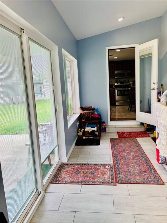 doorway to outside featuring tile patterned floors, baseboards, lofted ceiling, and a healthy amount of sunlight