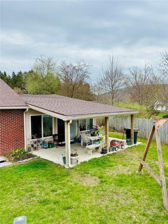 back of property featuring fence, a shingled roof, a yard, and a patio area