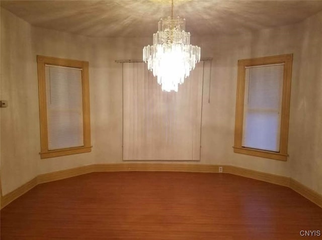 spare room featuring an inviting chandelier, wood finished floors, and baseboards