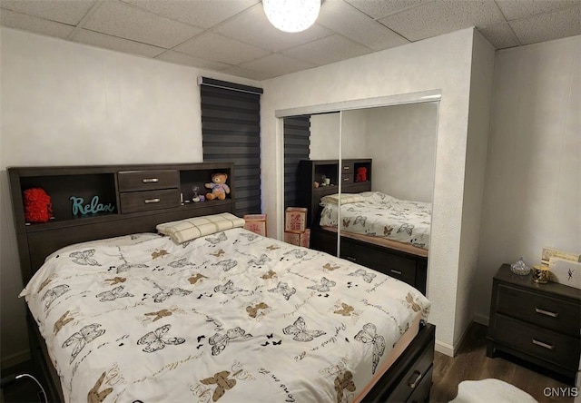bedroom featuring dark wood finished floors, baseboards, a closet, and a paneled ceiling