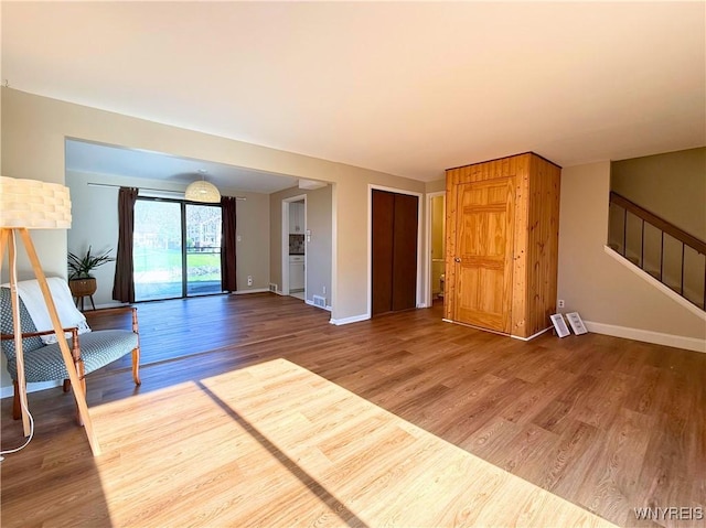 unfurnished living room featuring stairway, wood finished floors, visible vents, and baseboards