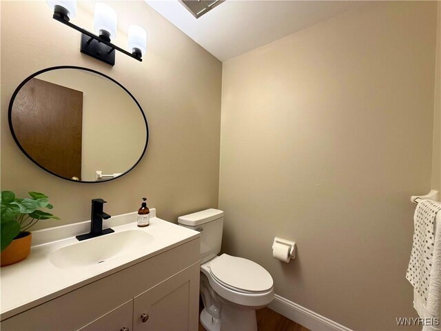 half bathroom featuring baseboards, wood finished floors, toilet, and vanity