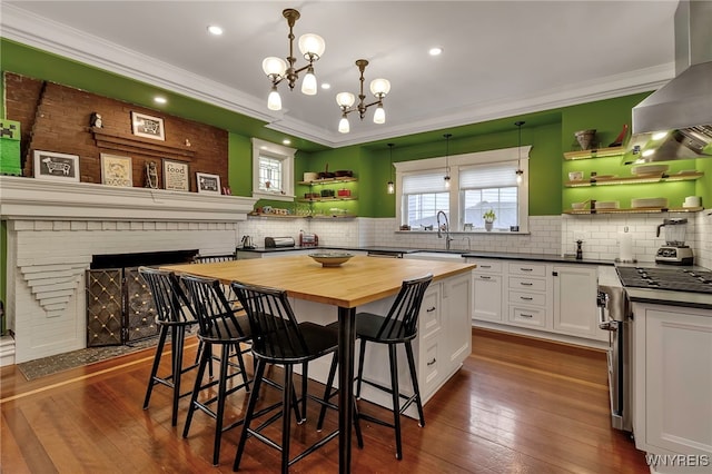 kitchen with wood counters, open shelves, wall chimney range hood, a sink, and crown molding