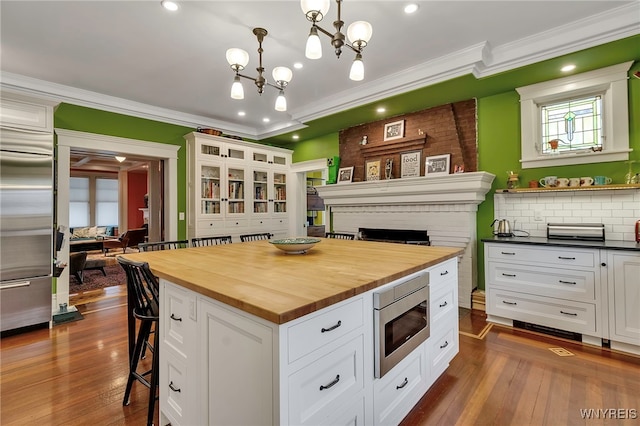kitchen featuring wood counters, built in appliances, a kitchen bar, ornamental molding, and a fireplace