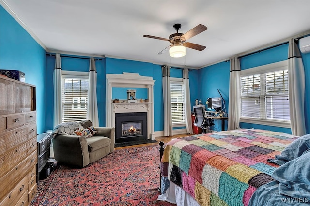 bedroom featuring multiple windows, wood finished floors, a fireplace with flush hearth, and crown molding