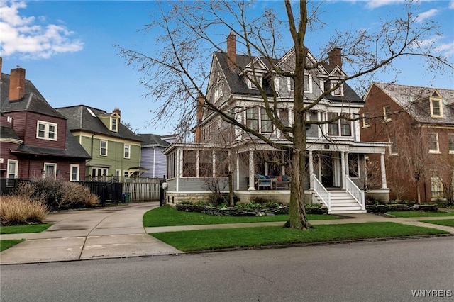 view of front facade with a sunroom, a residential view, covered porch, a chimney, and fence