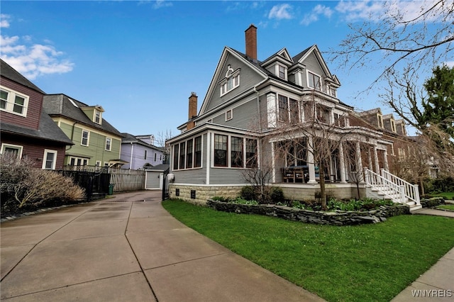 victorian house with a chimney, fence, an outdoor structure, and a front yard
