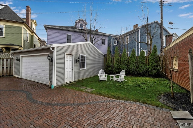 back of house featuring fence, decorative driveway, a lawn, and an attached garage
