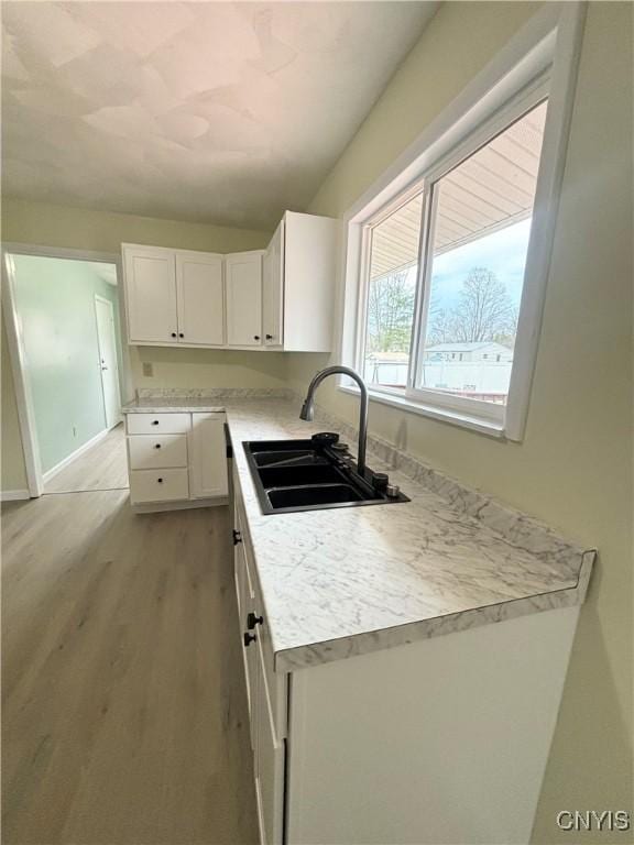kitchen with light wood finished floors, a sink, white cabinetry, and light countertops