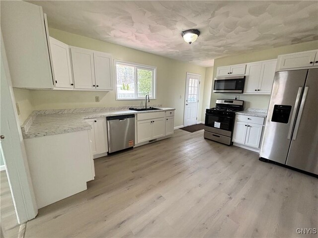 kitchen featuring appliances with stainless steel finishes, light wood-style floors, white cabinetry, and a sink
