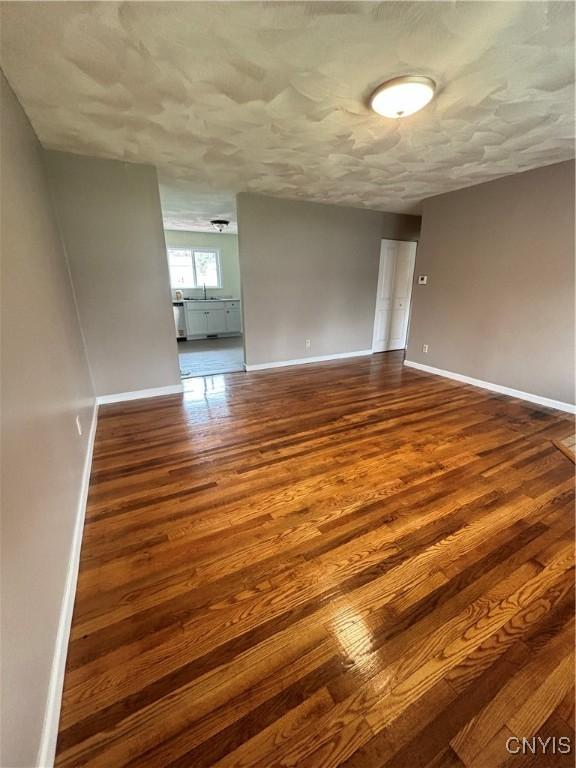 empty room featuring dark wood-style floors, a sink, and baseboards