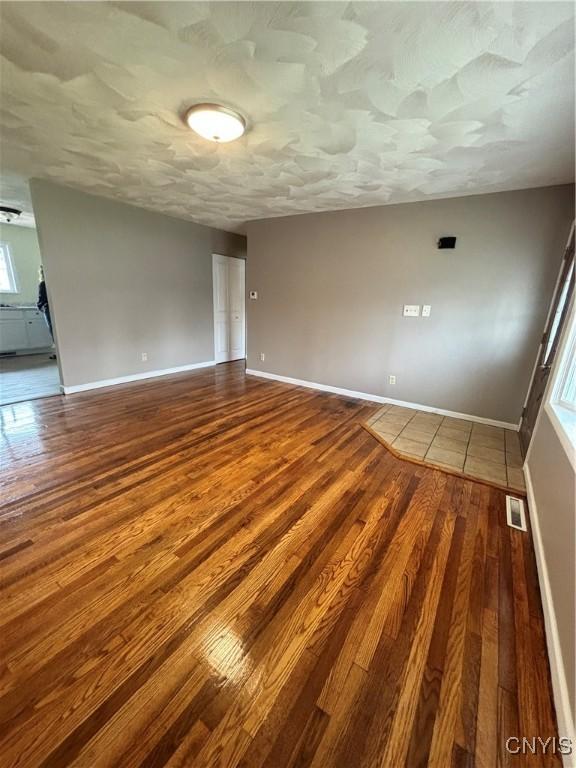 unfurnished room with dark wood finished floors, baseboards, visible vents, and plenty of natural light