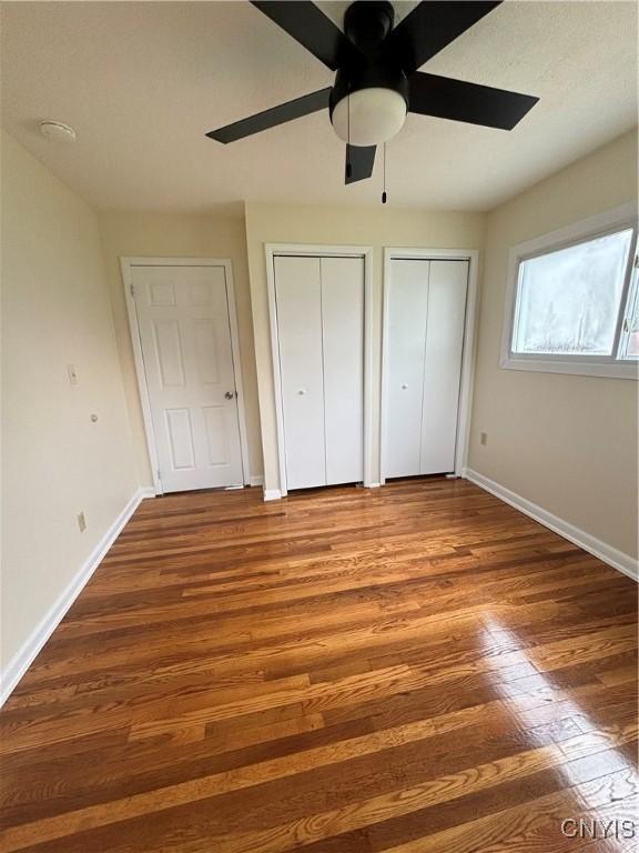 unfurnished bedroom featuring a ceiling fan, two closets, wood finished floors, and baseboards