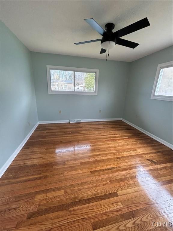 spare room featuring wood finished floors, visible vents, a ceiling fan, and baseboards