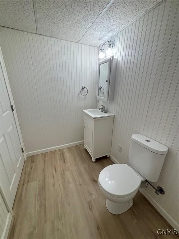 half bath featuring toilet, vanity, wood walls, and wood finished floors