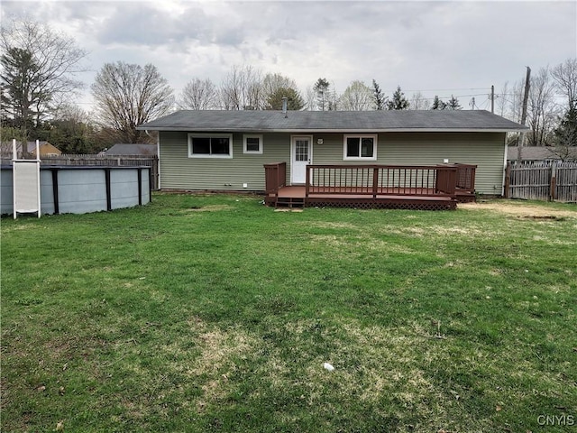 back of property featuring fence, a wooden deck, a swimming pool, and a yard
