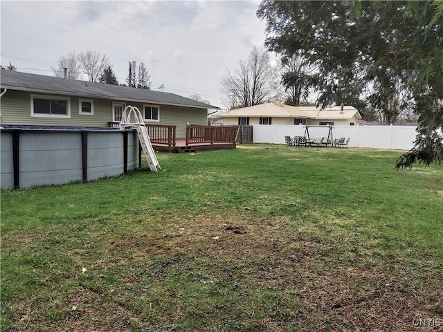 view of yard with a wooden deck, a swimming pool, and fence