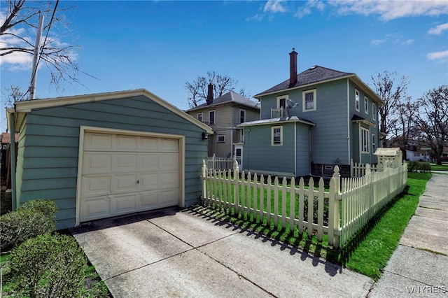 exterior space featuring driveway, a chimney, a detached garage, an outbuilding, and a fenced front yard
