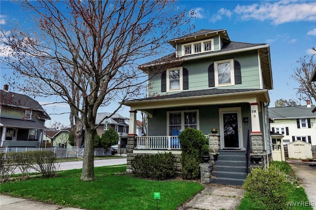 american foursquare style home with a storage shed, covered porch, and fence