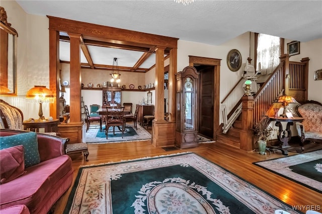living room with stairway, beam ceiling, wood finished floors, and ornate columns