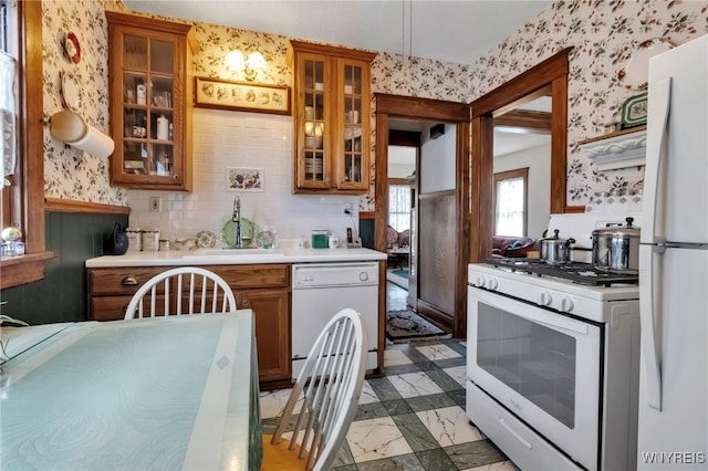 kitchen featuring a sink, brown cabinets, white appliances, light countertops, and wallpapered walls