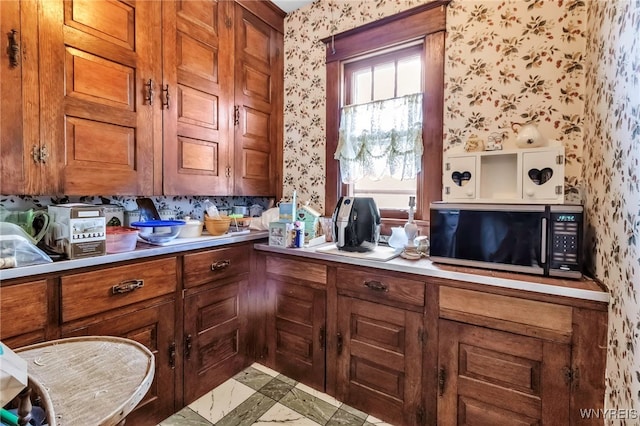 kitchen featuring black microwave, brown cabinets, wallpapered walls, and light countertops