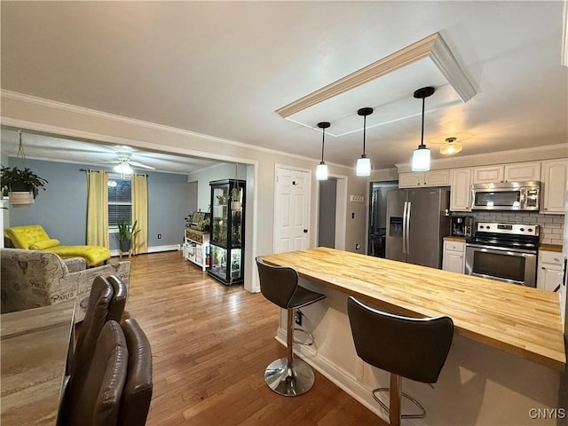 kitchen featuring decorative backsplash, appliances with stainless steel finishes, open floor plan, a kitchen bar, and butcher block countertops