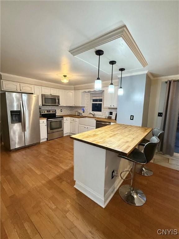 kitchen with tasteful backsplash, butcher block countertops, hardwood / wood-style floors, stainless steel appliances, and white cabinets