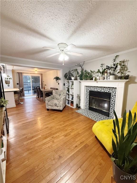 living area featuring crown molding, a tile fireplace, a textured ceiling, and light wood-type flooring