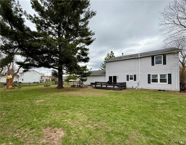 rear view of house featuring fence, a wooden deck, a playground, and a lawn