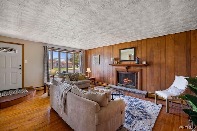 1631 Tuscarora Rd, Niagara, NY 14304 - living room featuring a textured ceiling, wood walls, a baseboard radiator, a warm lit fireplace, and wood finished floors