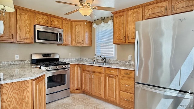 kitchen with brown cabinets, a sink, stainless steel appliances, light stone countertops, and a ceiling fan